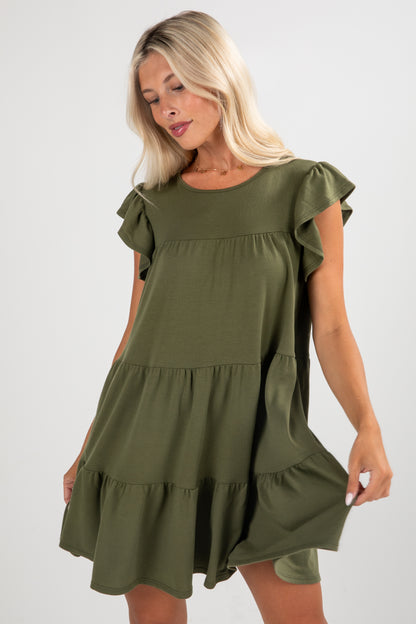 Woman wearing an olive green dress with ruffled sleeves and bottom hem on a white background