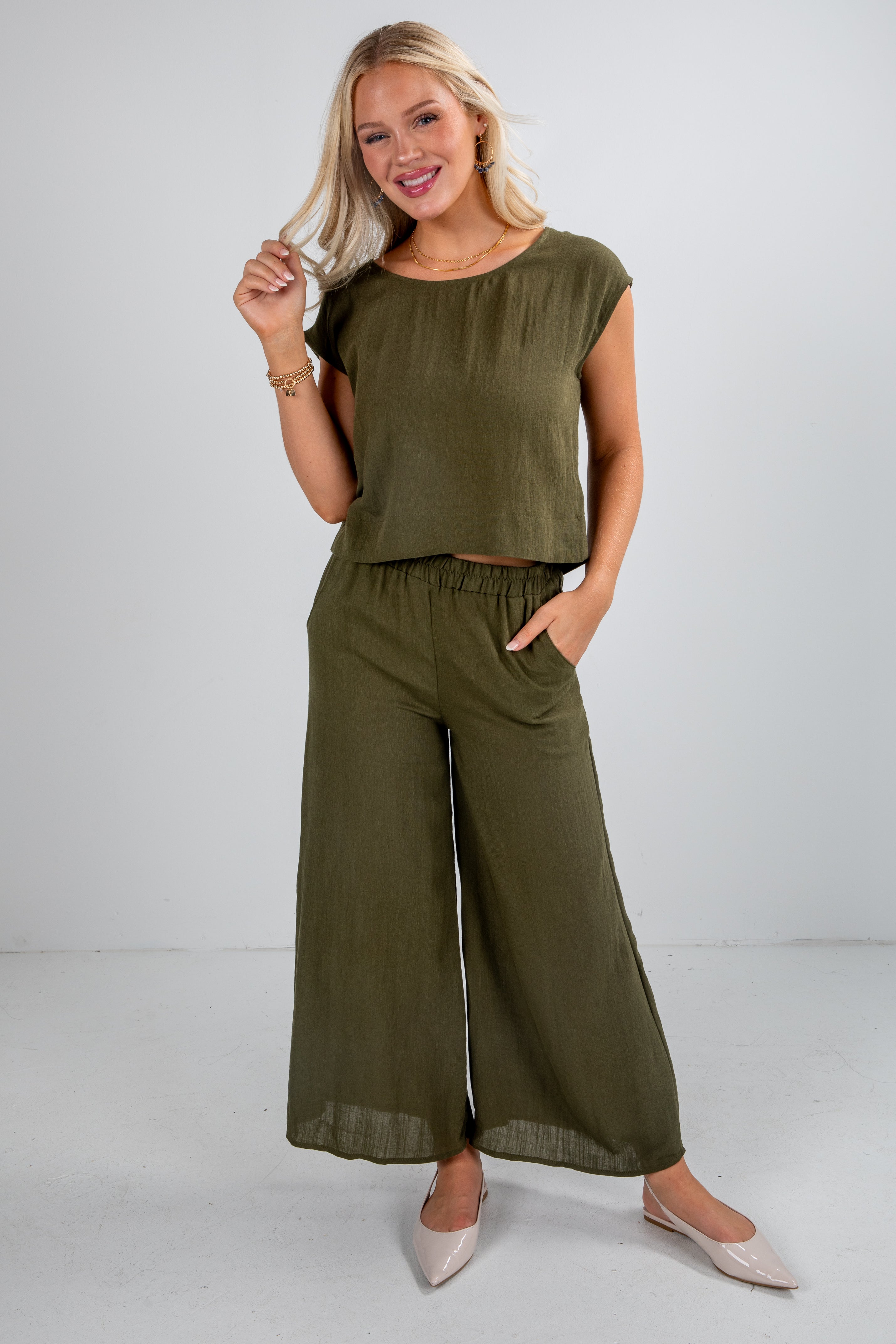 Woman wearing an olive green top and wide-leg pants on a white background