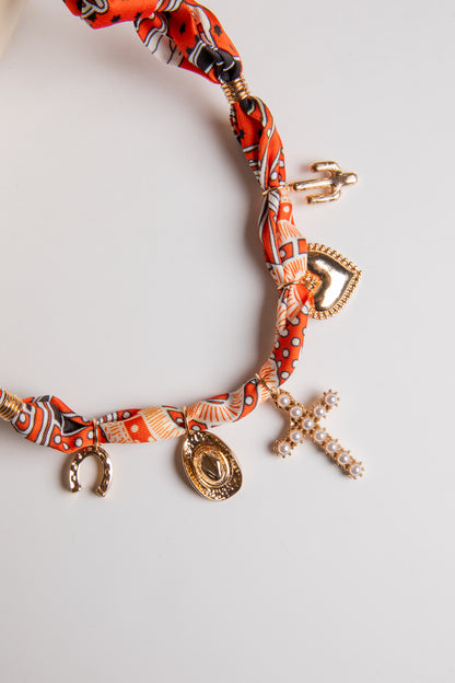 Necklace with orange patterned fabric and charms on a light gray background