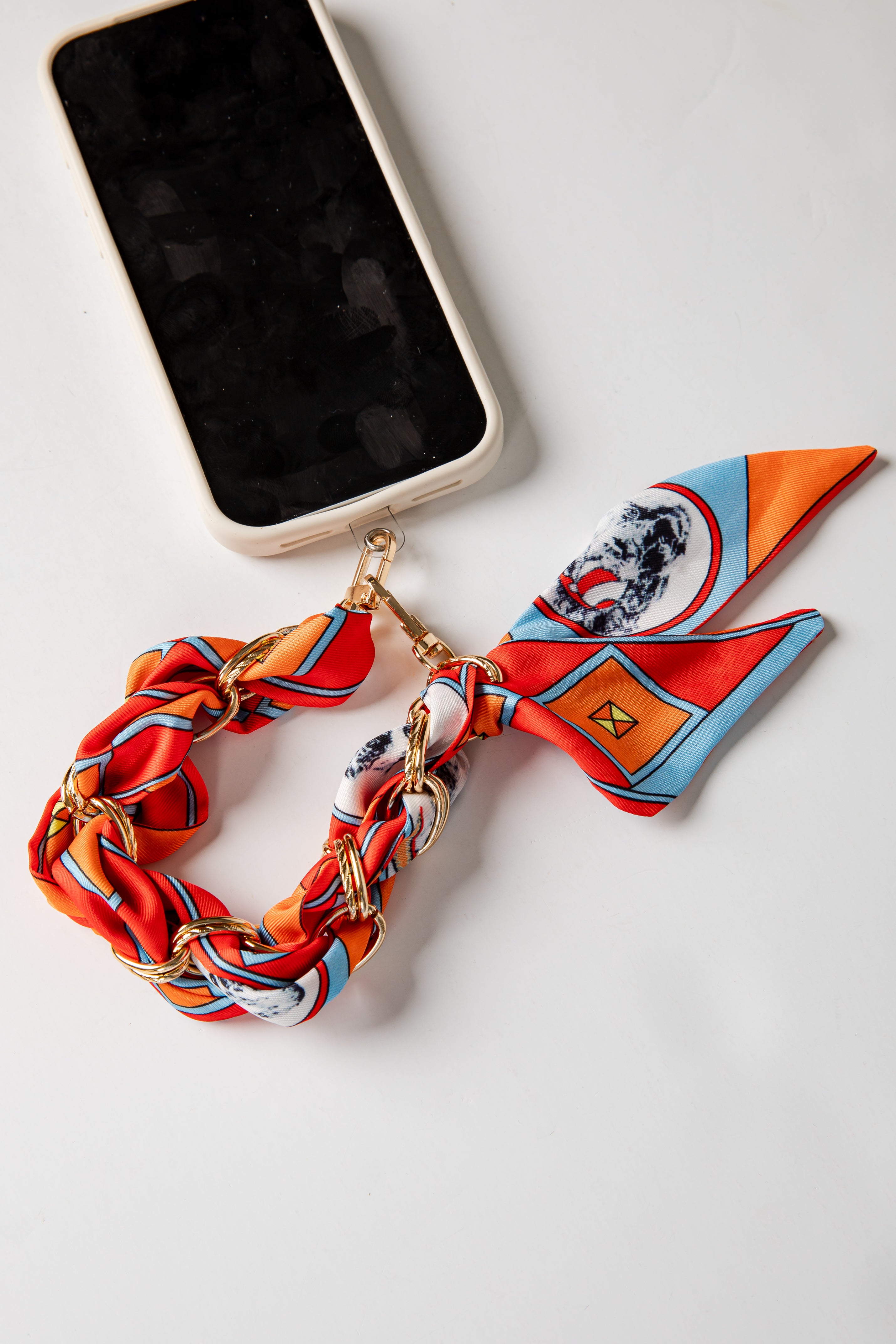 Colorful scarf with a bow tie design draped over a phone on a white background
