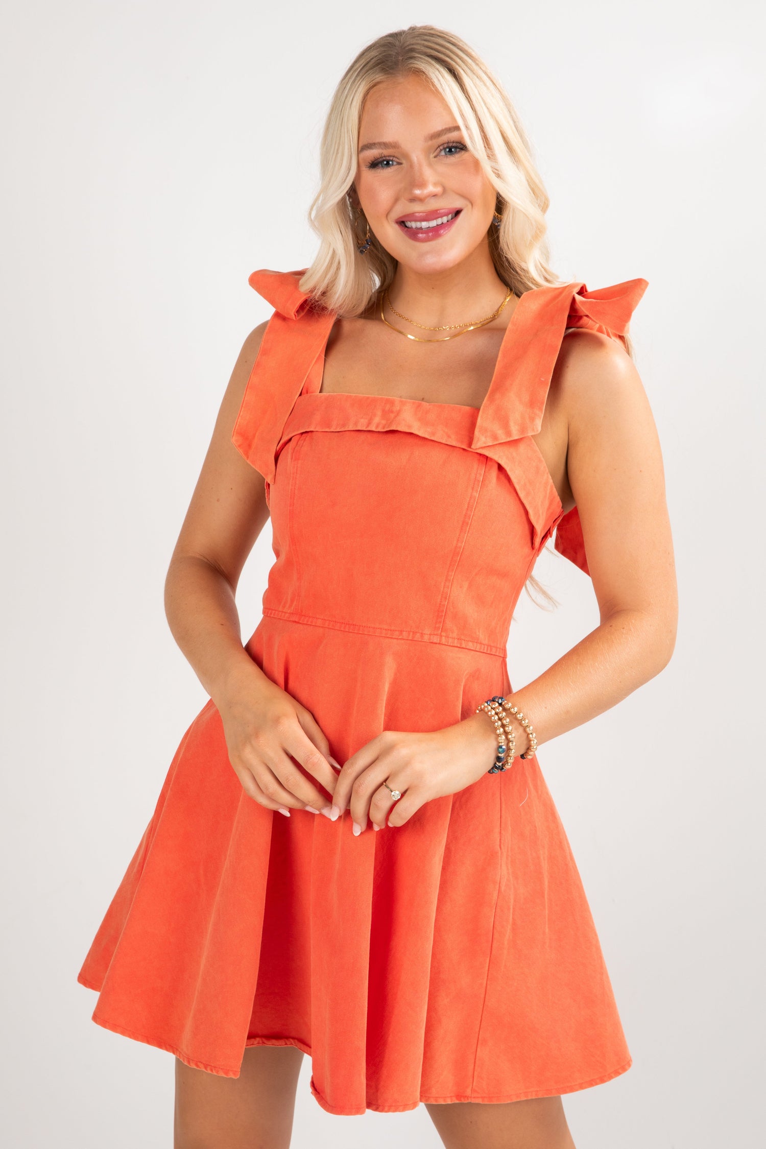 Woman wearing an orange dress with ruffled shoulders on a white background