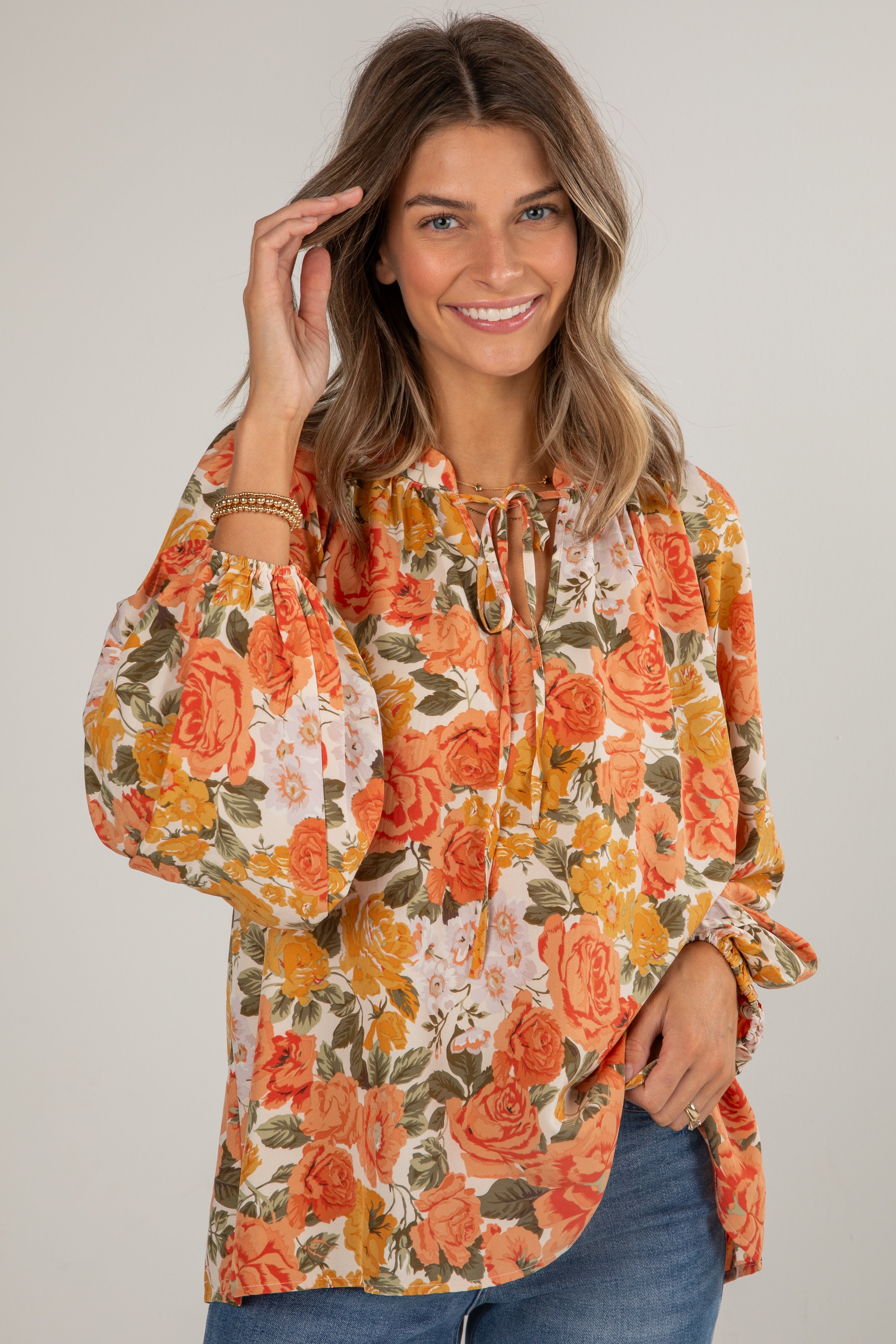 Woman wearing a floral blouse with orange and green flowers on a plain background
