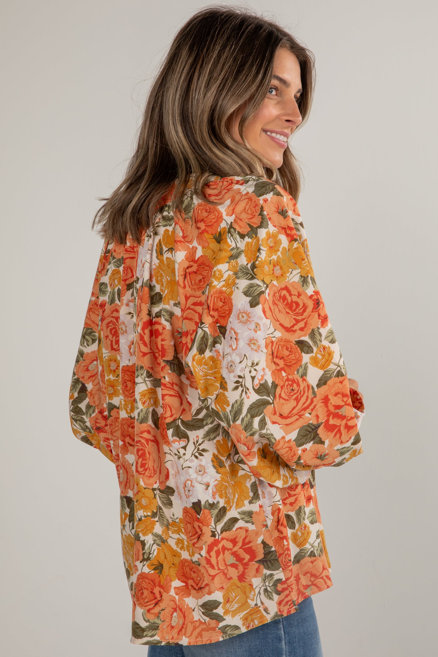 Woman wearing a floral blouse with orange and yellow flowers on a plain background