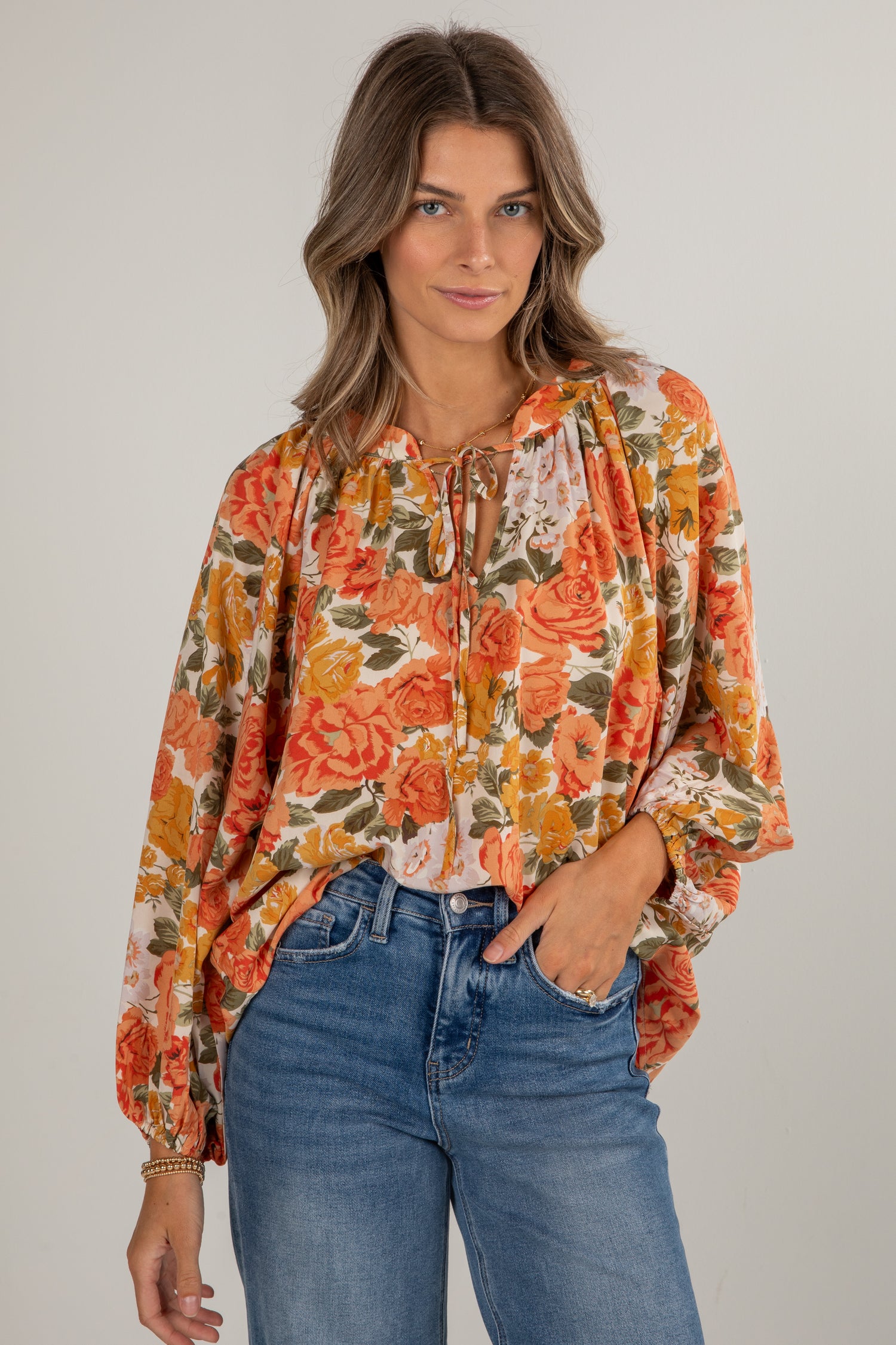 Woman wearing a floral blouse and jeans on a plain background