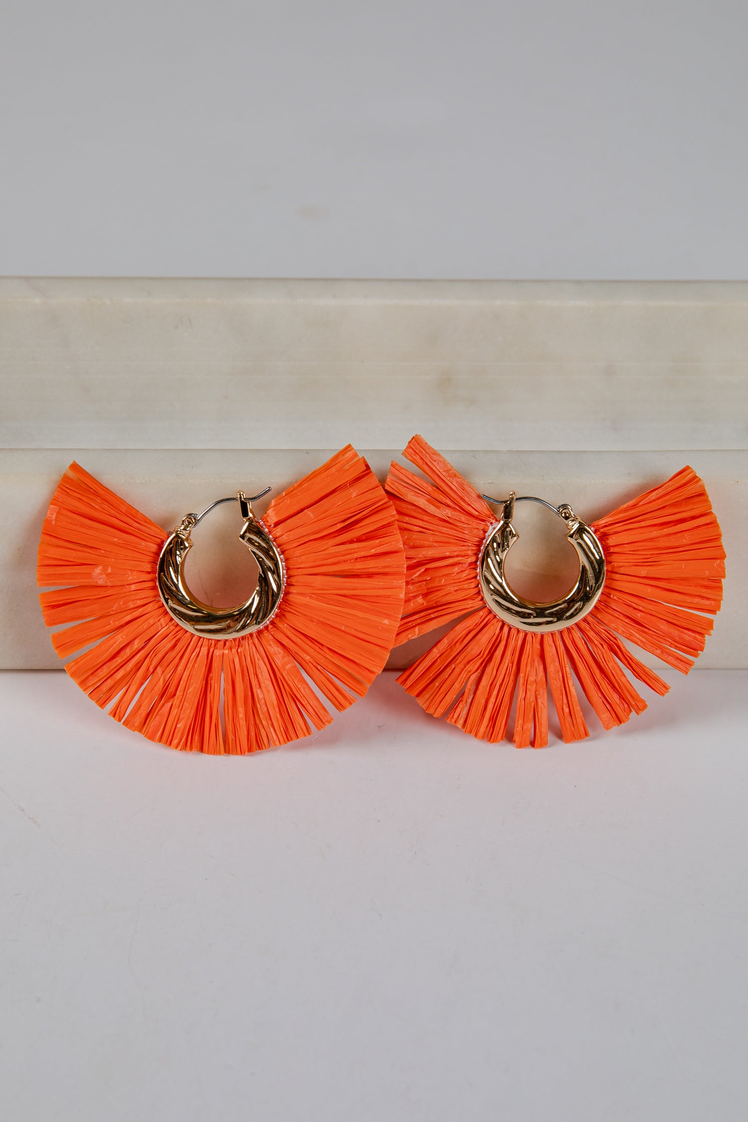 Orange ruffled earrings with gold hoops on a light background