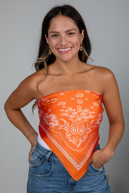 Woman wearing an orange bandana top with white patterns on a gray background