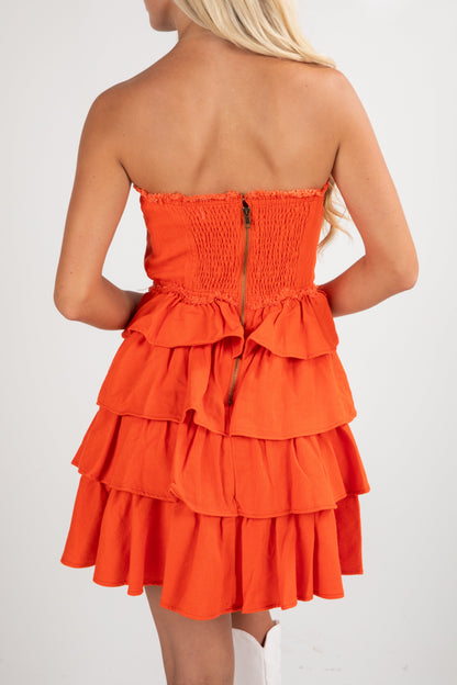 Orange strapless dress with ruffled layers on a white background