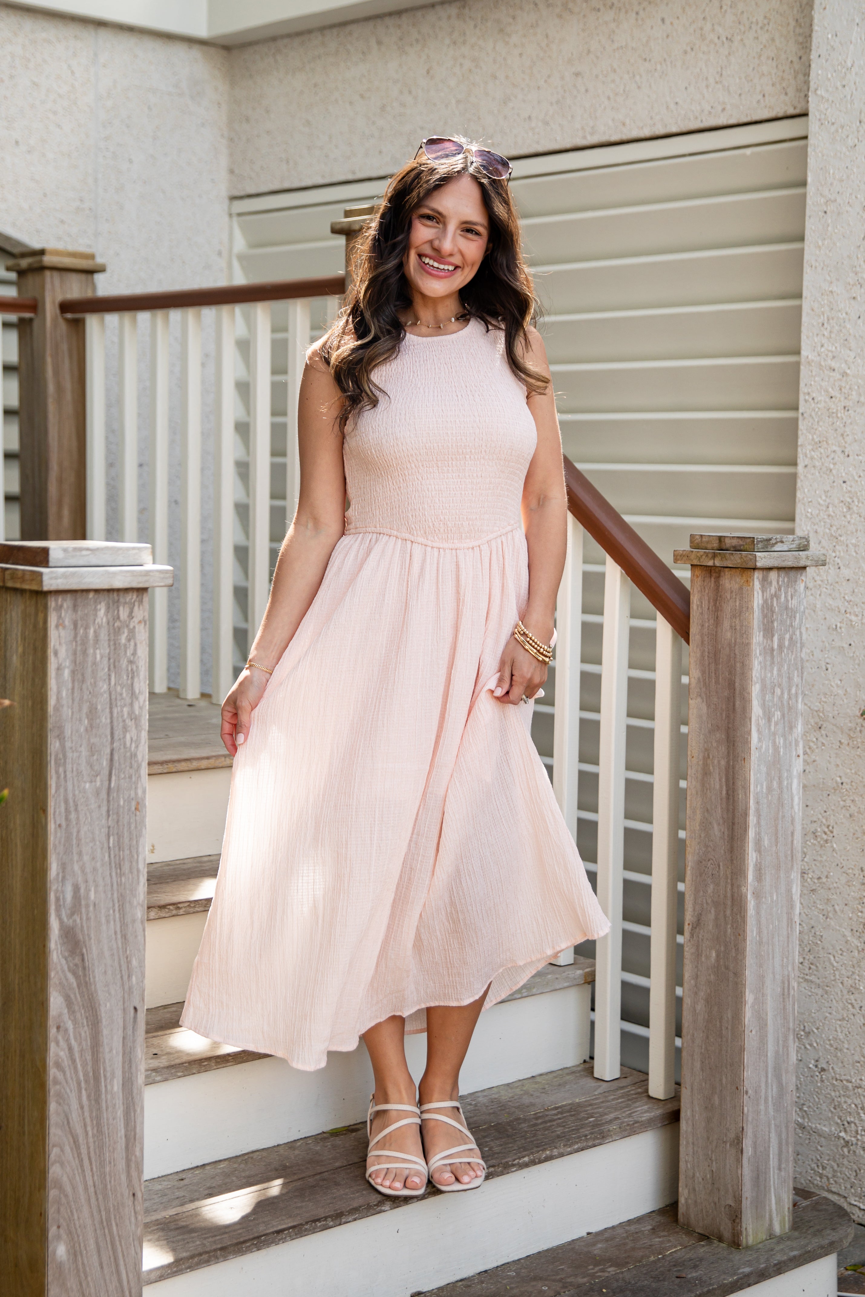 Woman in a light pink dress standing on wooden steps outside a house.