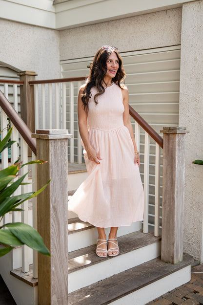 Woman in a light pink dress standing on wooden steps outside a house.