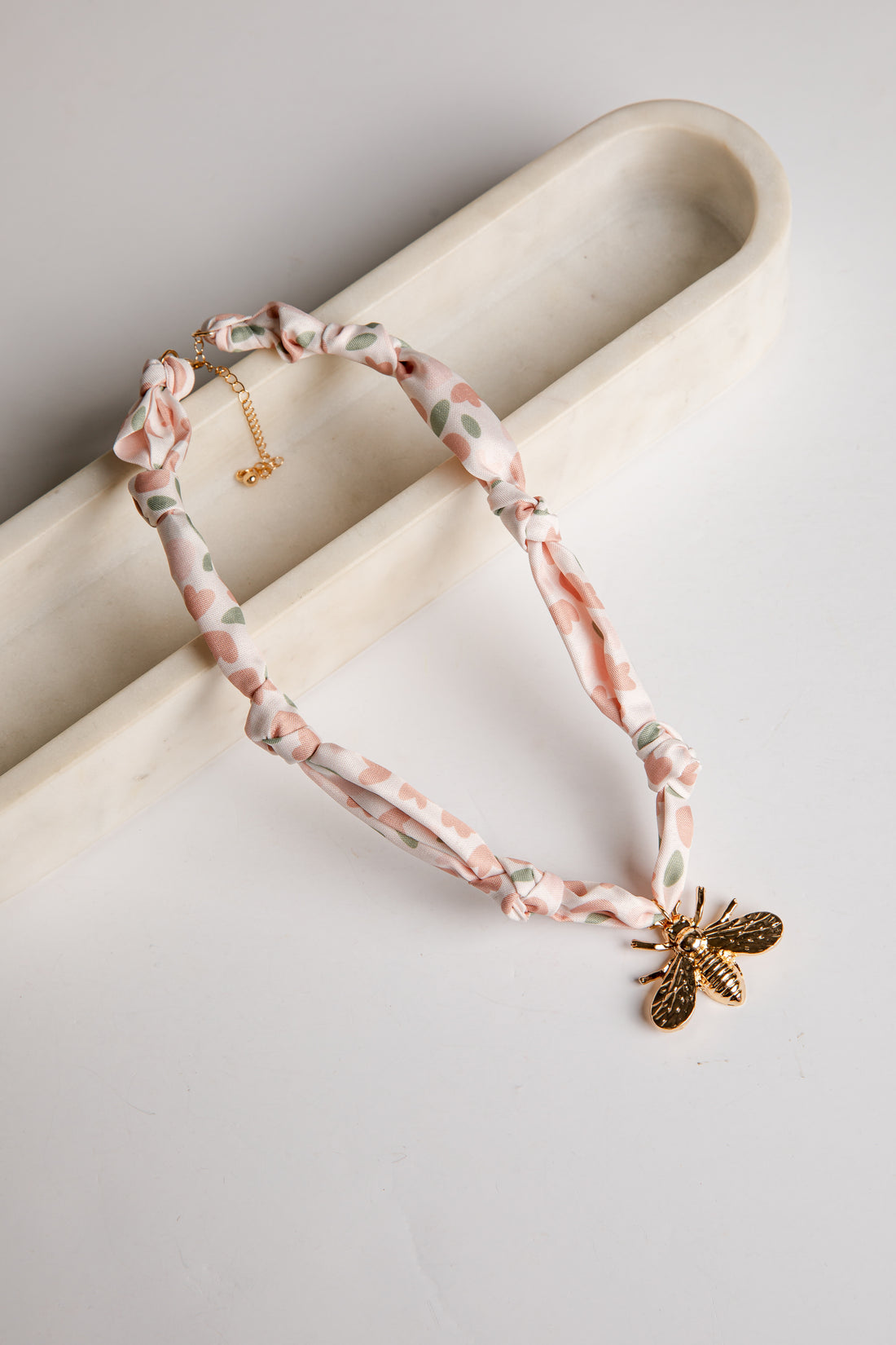Necklace with floral pattern and bee charm on a marble surface