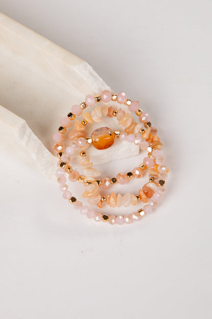 Set of beaded bracelets with peach and gold colors on a white surface