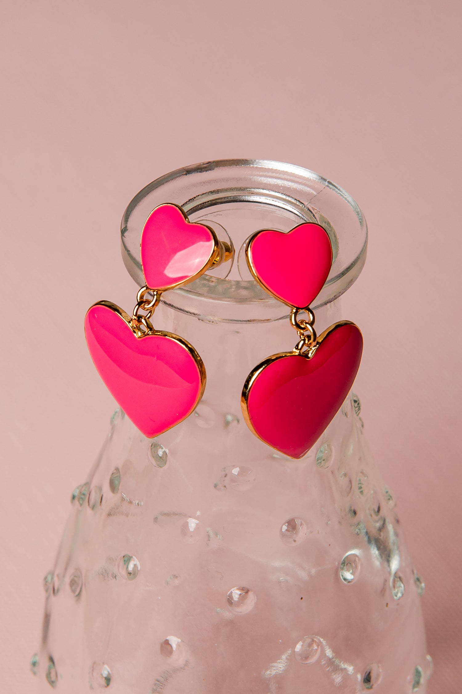 Pink heart-shaped earrings with gold accents on a pink background