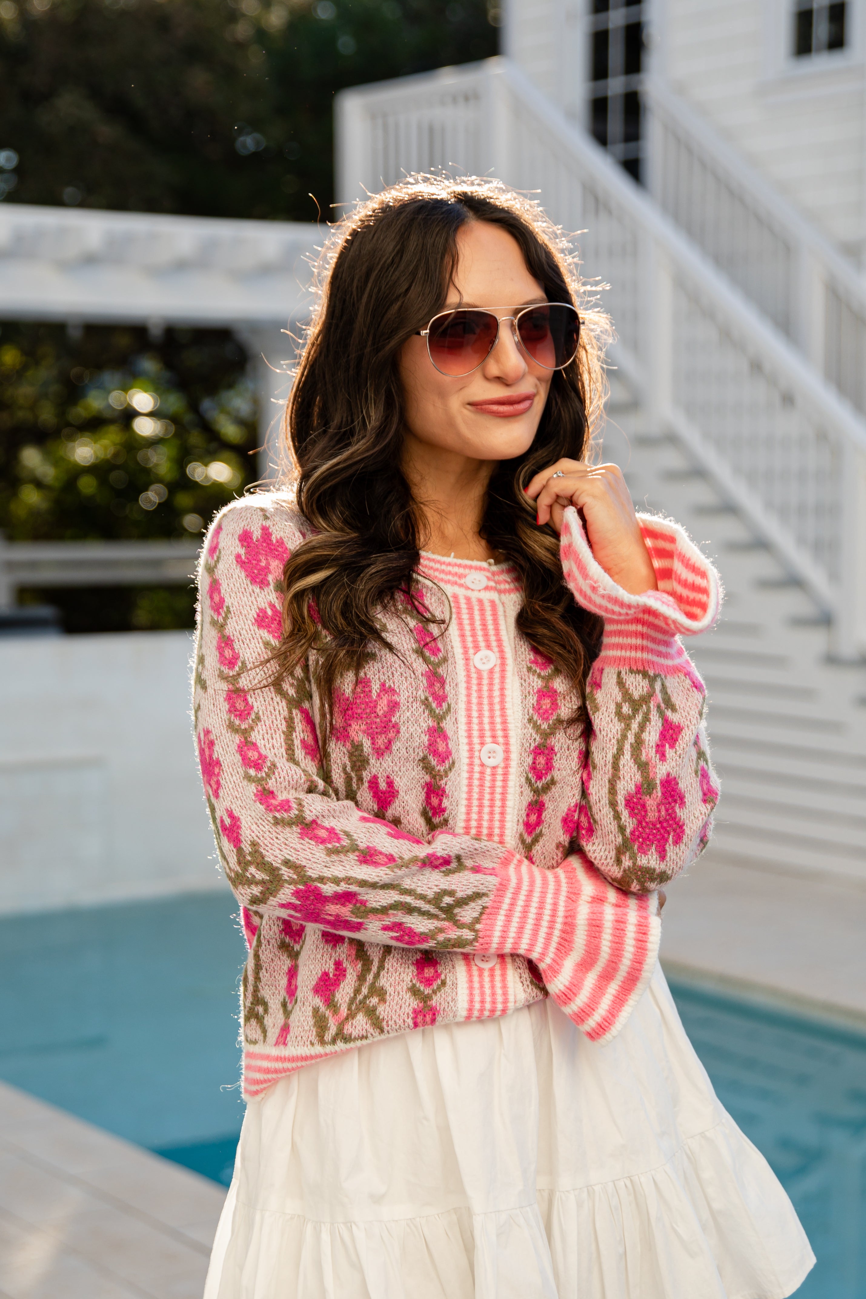 Woman wearing a colorful embroidered sweater and white skirt by a pool.