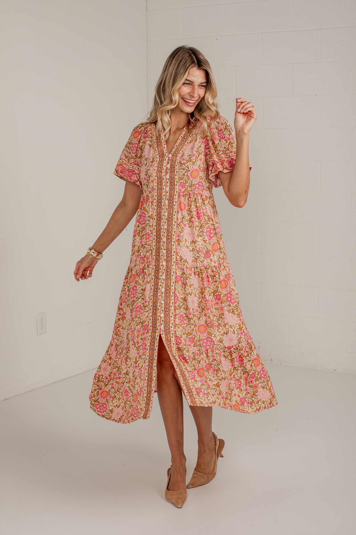 A woman modeling a short-sleeve midi dress with a pink, orange, and yellow floral print, standing in a bright white studio.