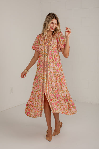 A woman modeling a short-sleeve midi dress with a pink, orange, and yellow floral print, standing in a bright white studio.