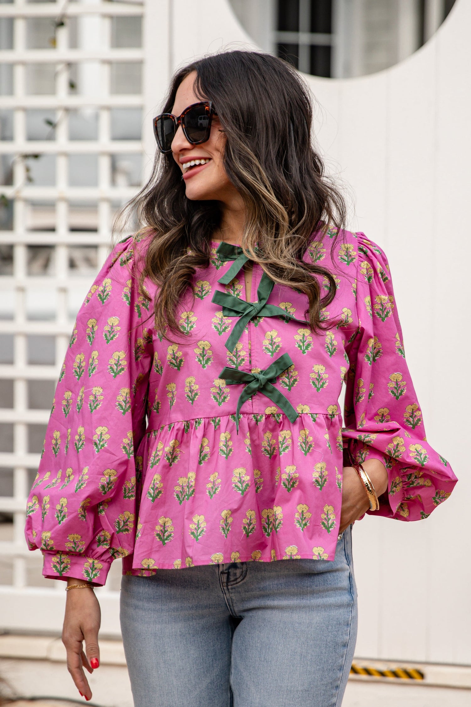 Woman wearing a pink blouse with floral patterns and green ribbons outdoors.