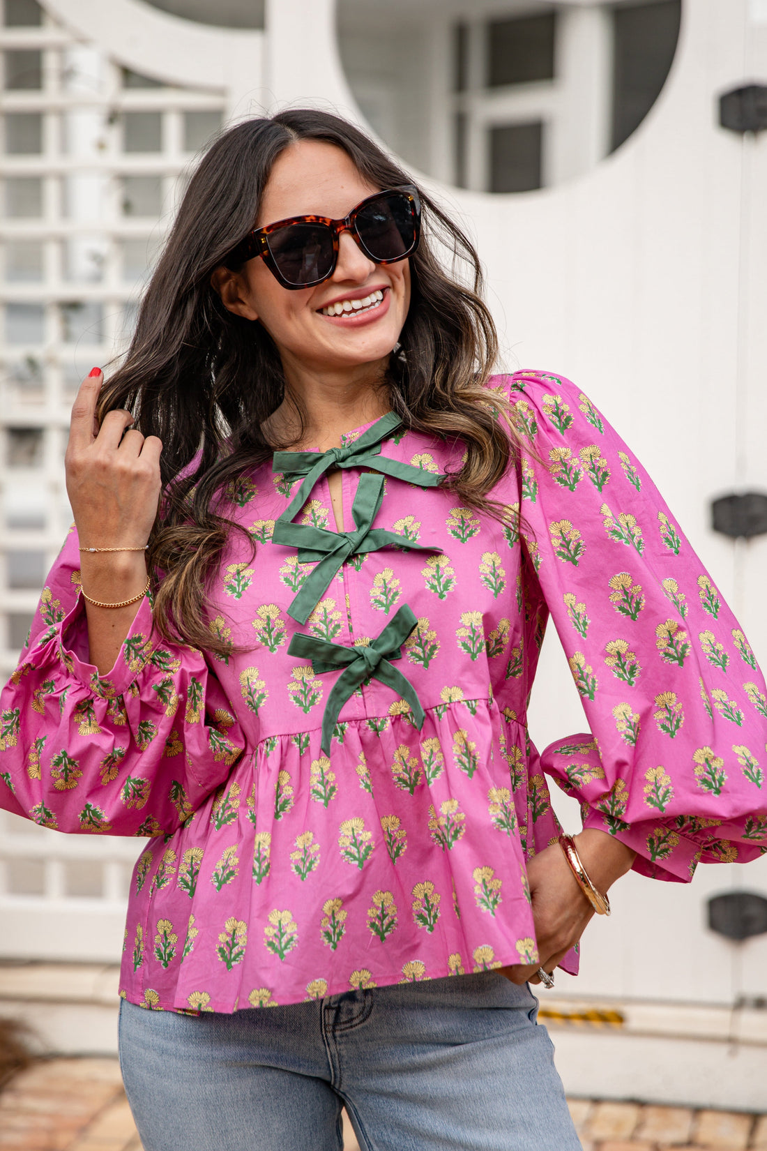 Woman wearing a pink floral blouse with green accents outdoors.
