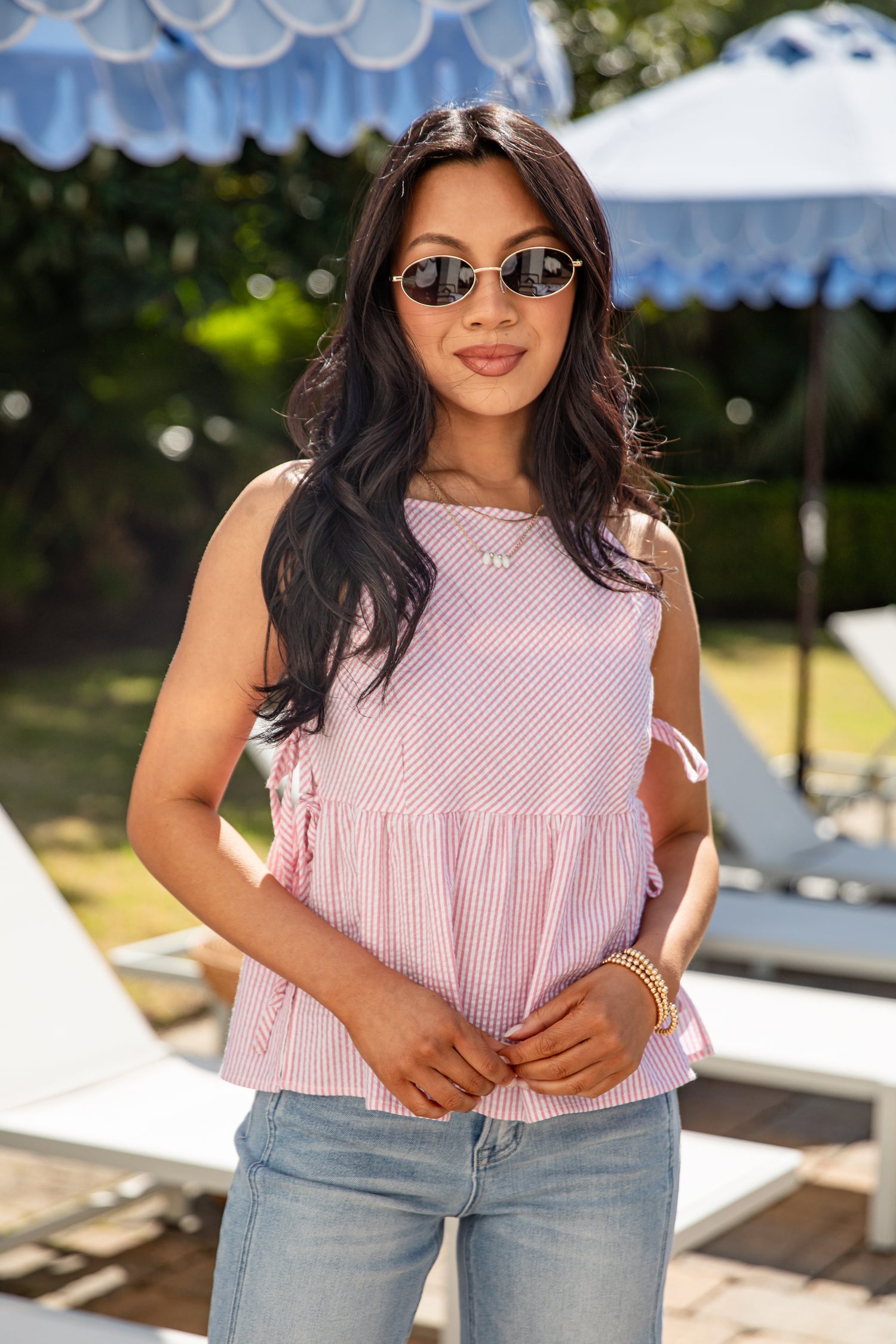Woman wearing a pink sleeveless top and sunglasses outdoors with blurred background