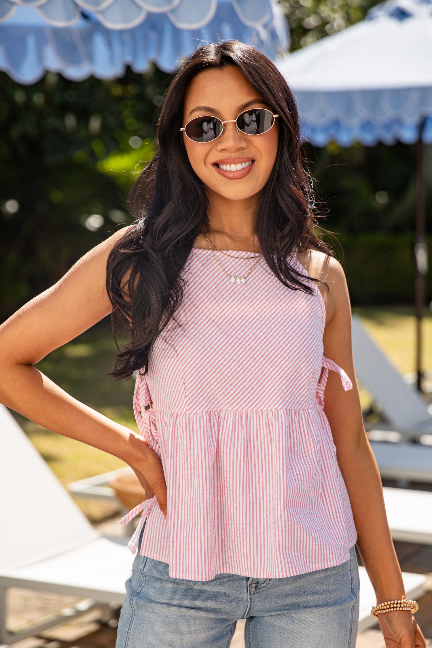 Woman wearing a pink striped top and sunglasses outdoors with umbrellas in the background
