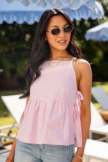 Woman wearing a pink striped sleeveless top with a blurred outdoor background