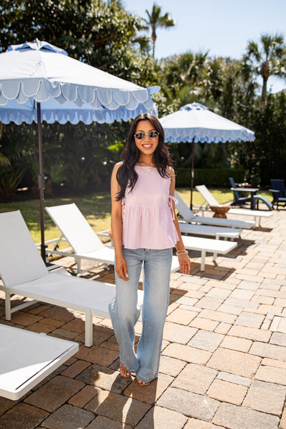 Woman standing in a sunlit outdoor setting with lounge chairs and umbrellas.