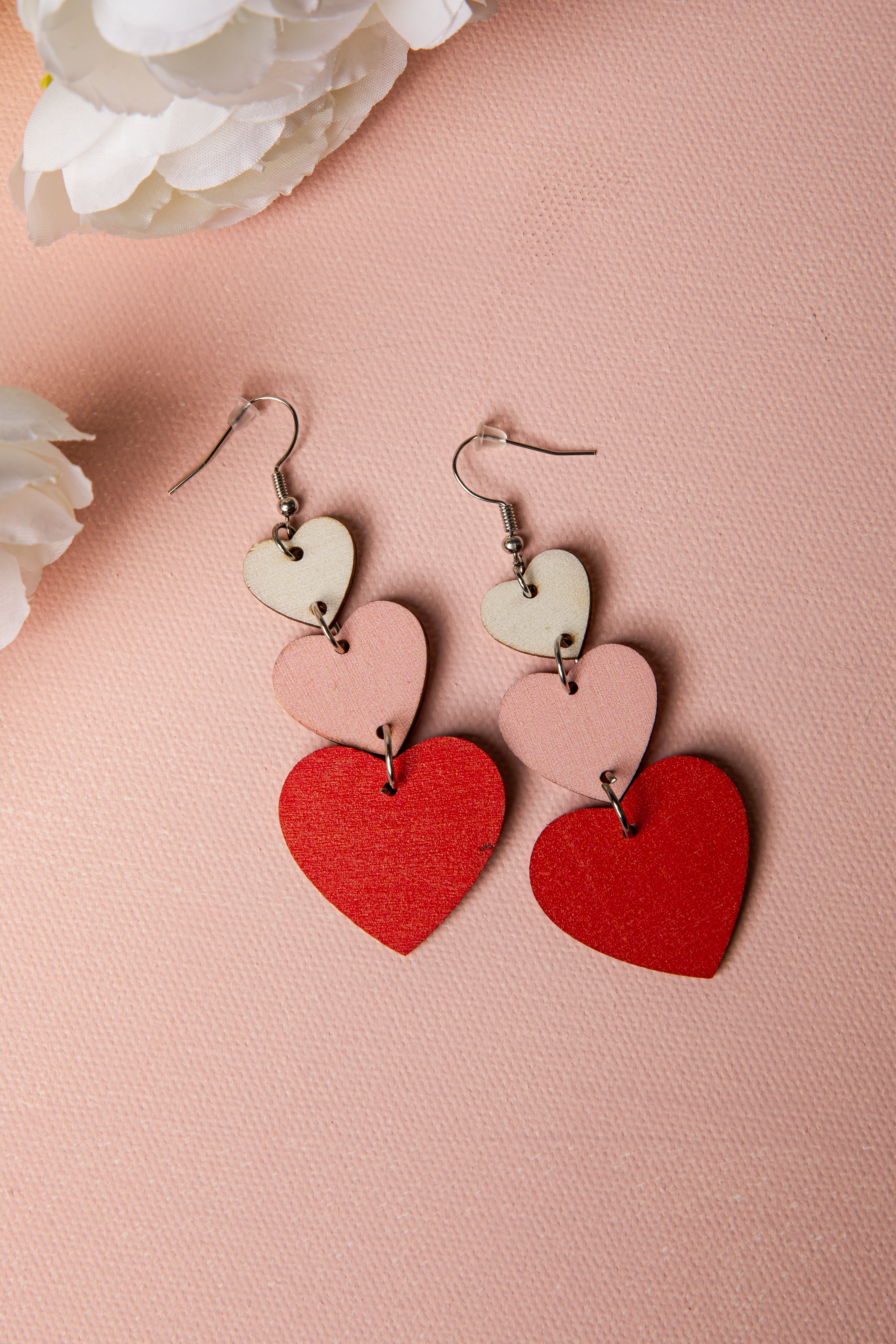 Heart-shaped earrings on a pink background with white flowers.