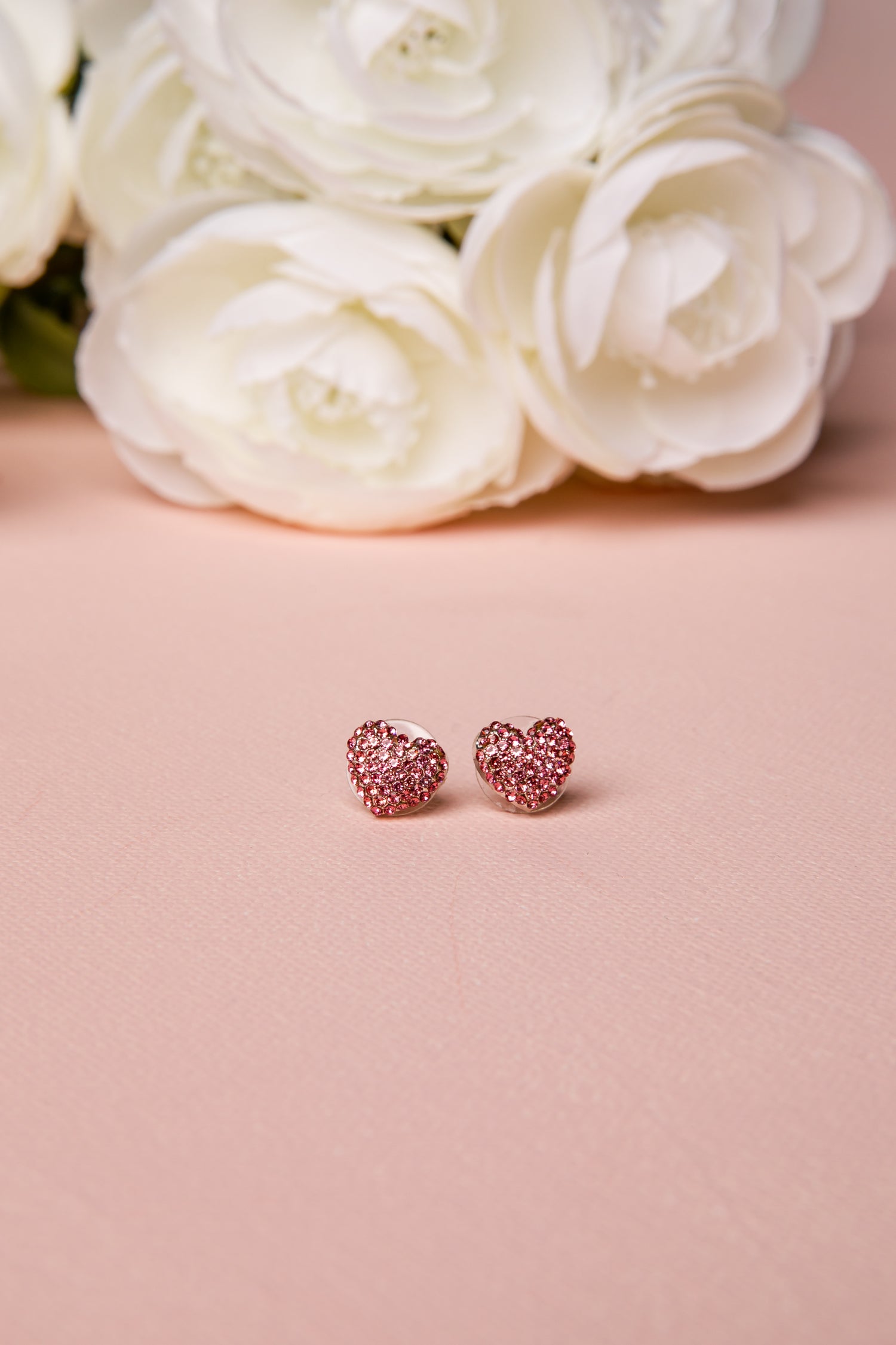 Pink heart-shaped earrings on a pink surface with white flowers in the background