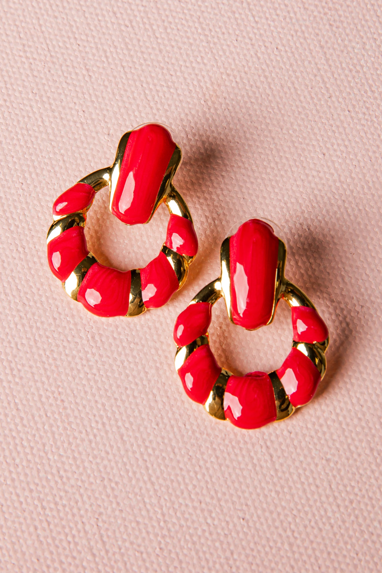 Red hoop earrings with gold accents on a pink background