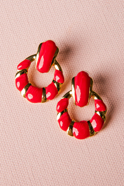 Red hoop earrings with gold accents on a pink background