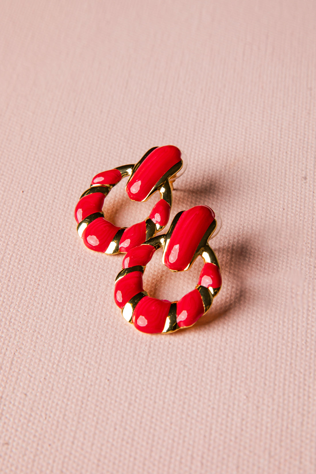 Red hoop earrings with gold accents on a pink background