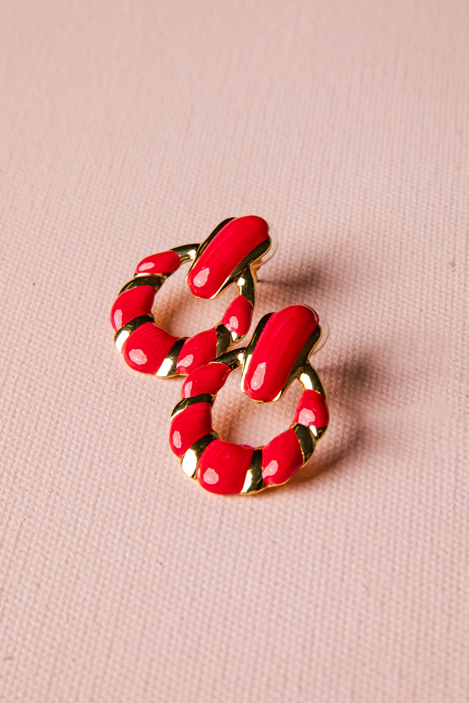 Red hoop earrings with gold accents on a pink background