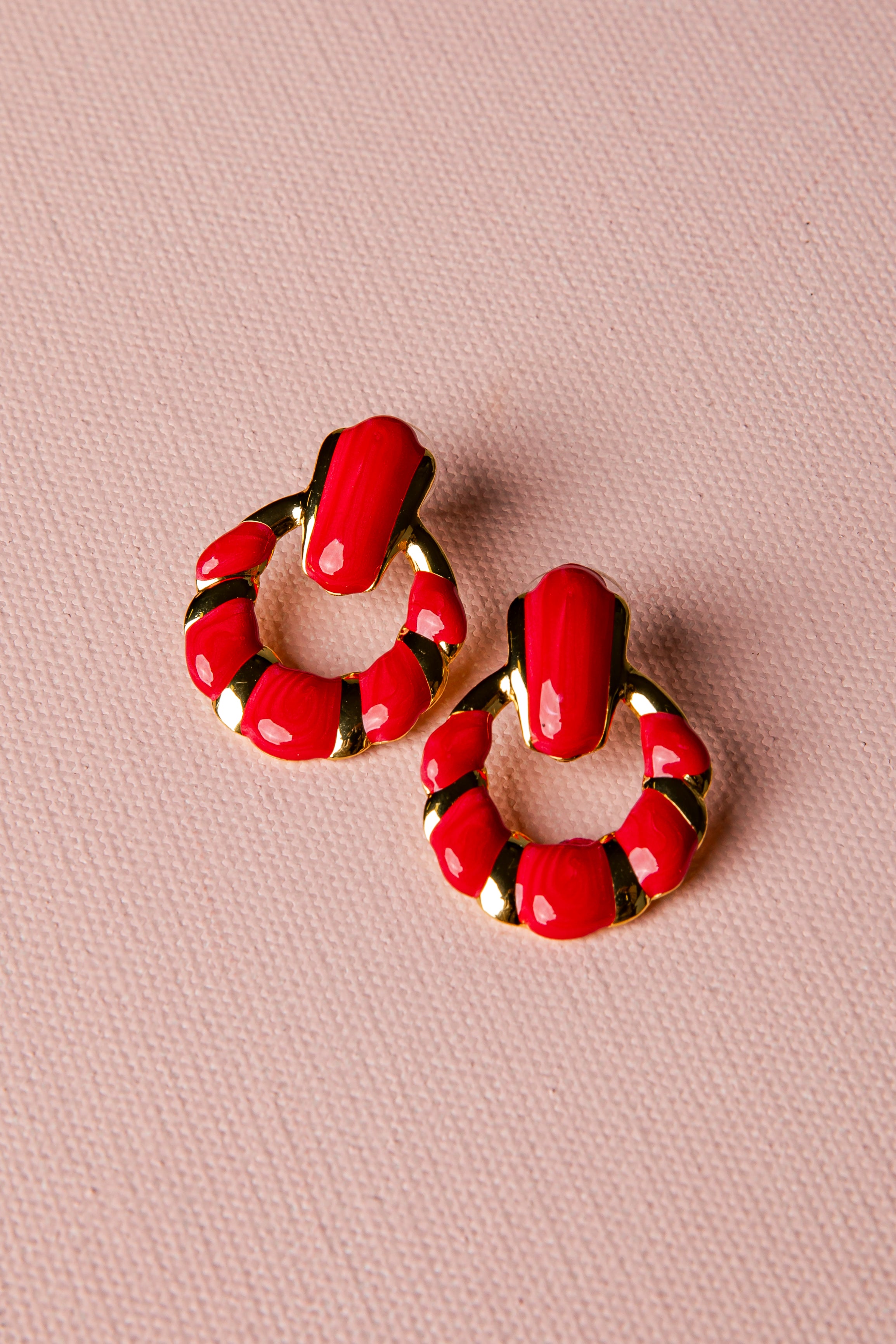 Red hoop earrings with gold accents on a pink background