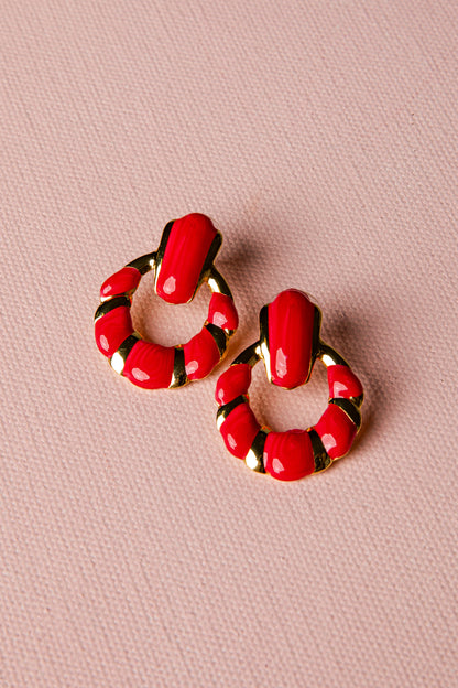 Red hoop earrings with gold accents on a pink background