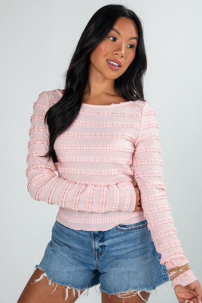 Woman wearing a pink textured sweater and denim shorts on a plain background