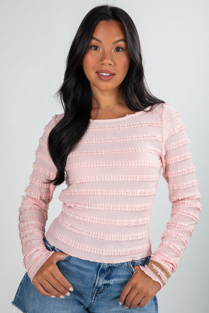Woman wearing a pink textured sweater and blue jeans on a plain background