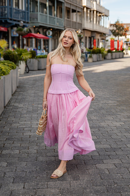 Woman in a pink strapless dress walking on a street with shops in the background