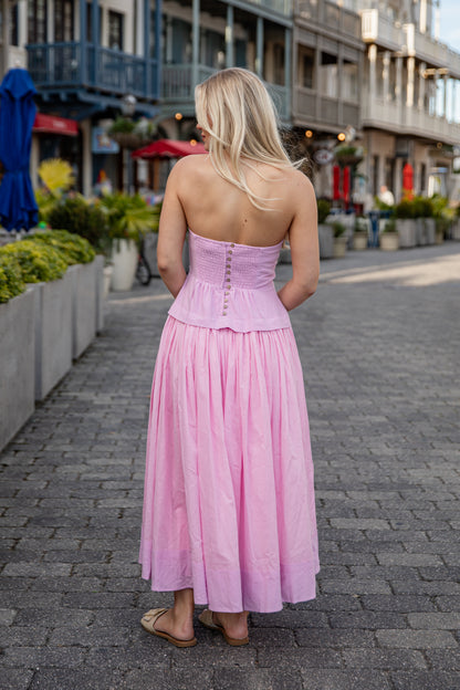 Woman in a pink dress walking on a street with shops and plants in the background