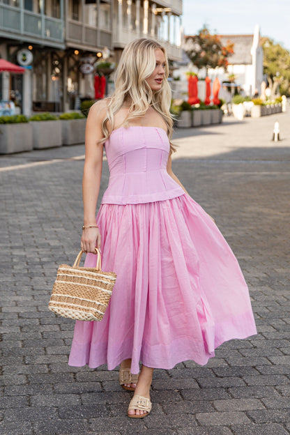 Woman in a pink dress walking on a street with buildings and trees in the background