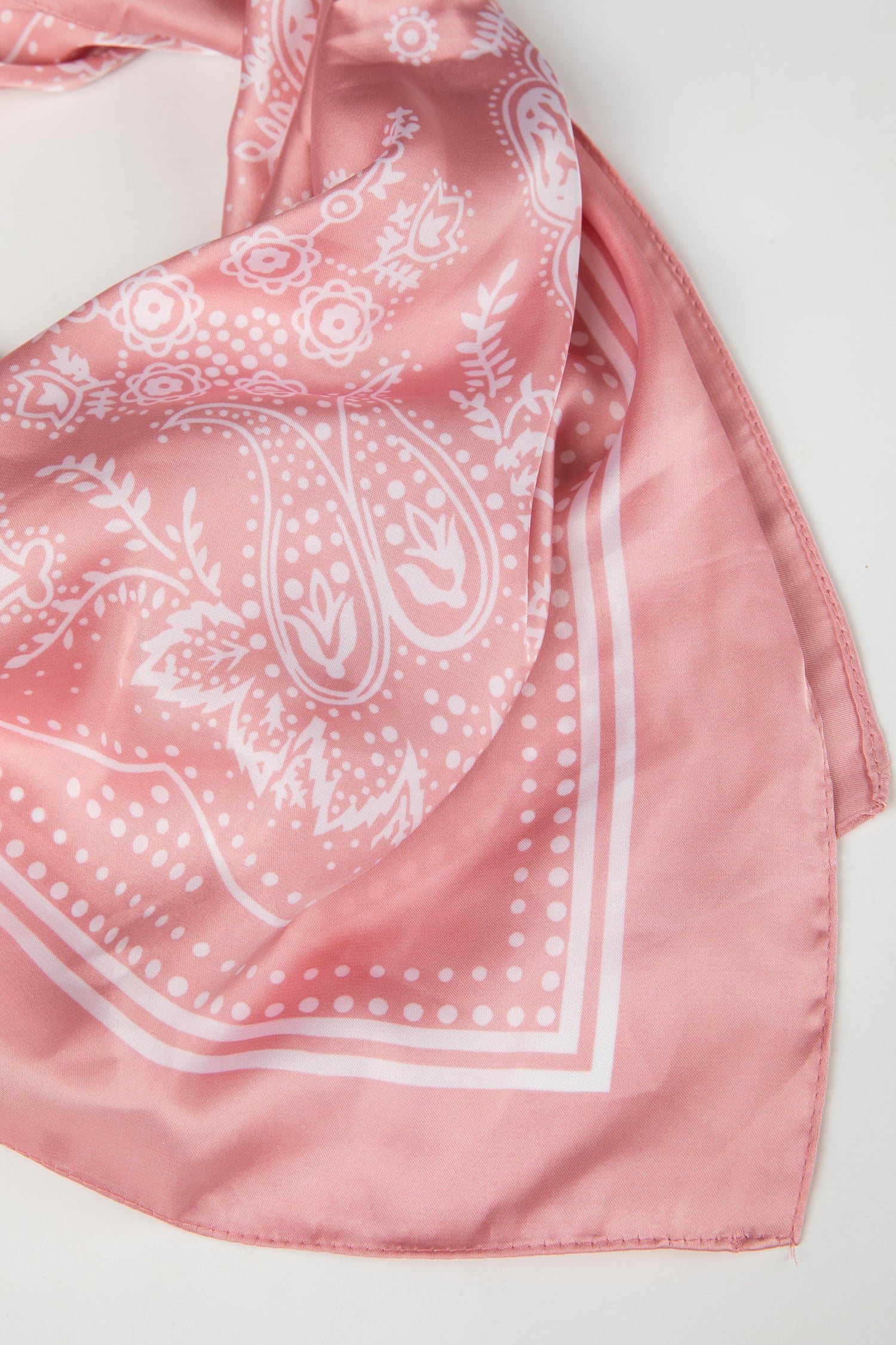 Pink bandana with white paisley pattern on a light gray background