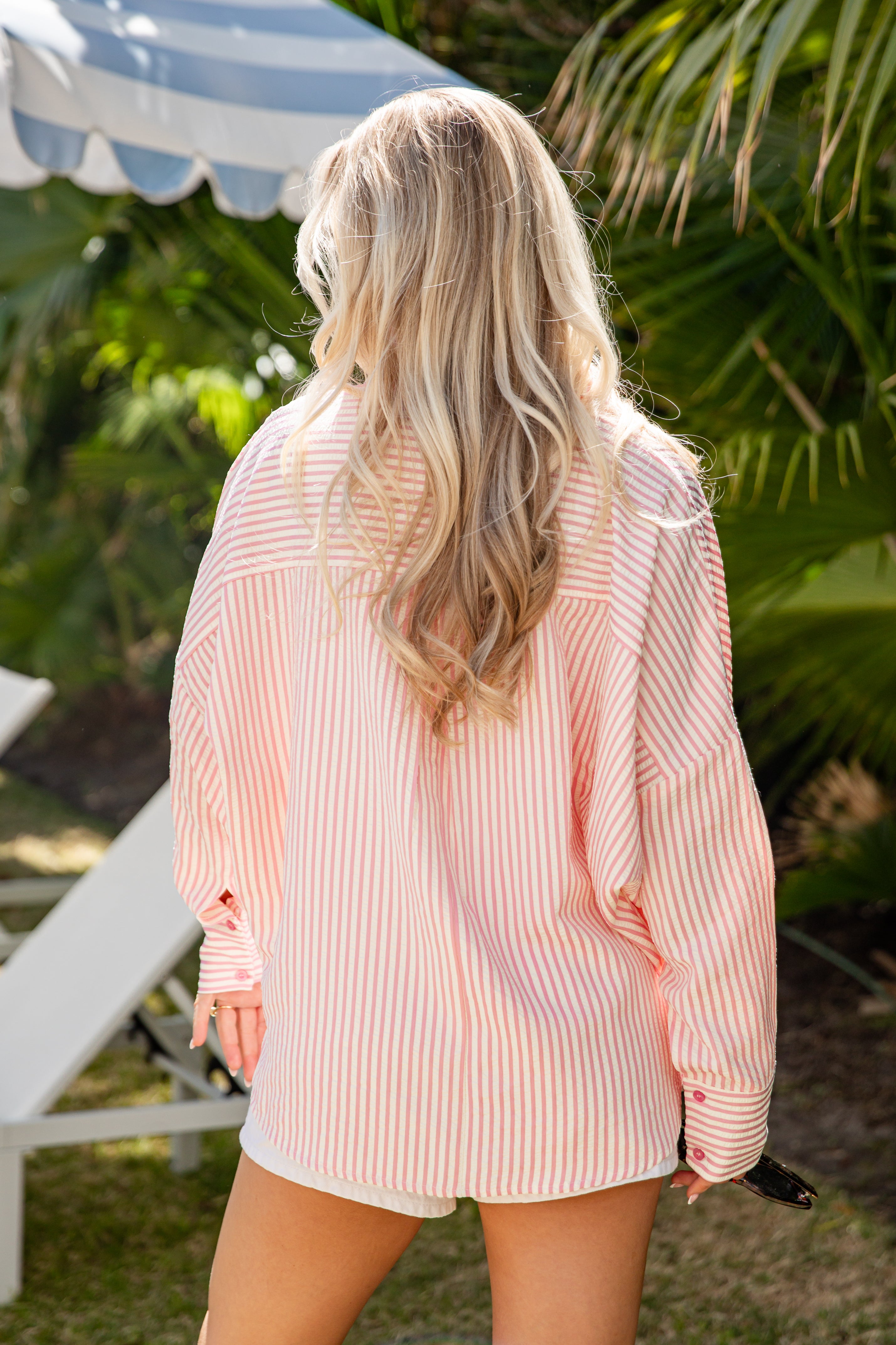 Woman wearing a pink and white striped shirt and shorts in an outdoor setting with greenery.