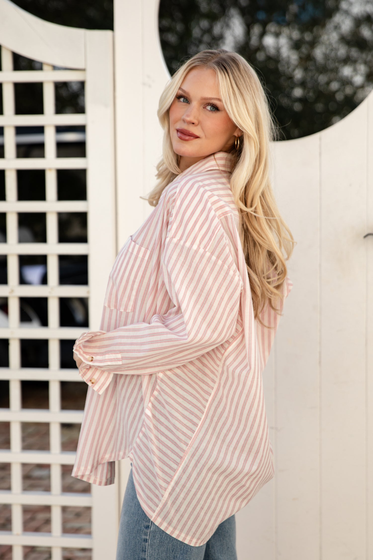 Woman wearing a light pink ribbed cardigan standing against a white lattice background