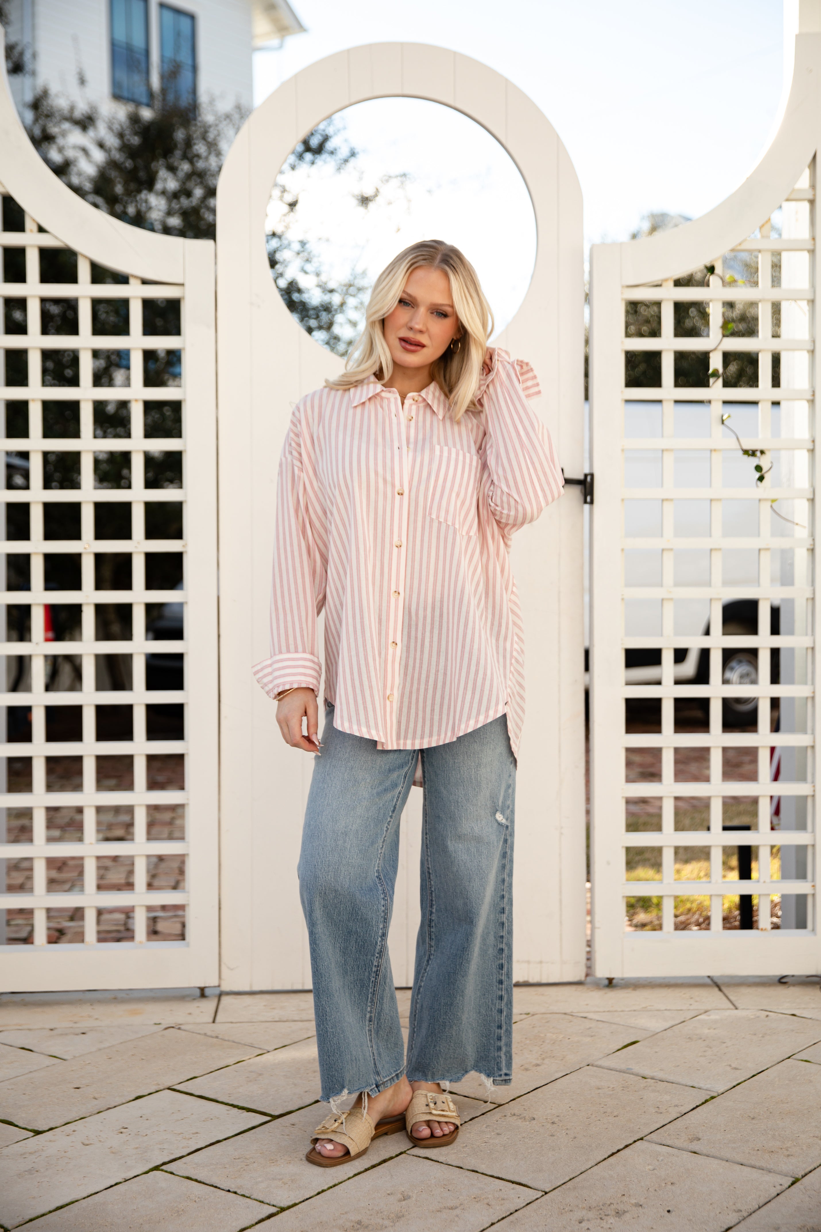 Woman standing in front of a white lattice gate wearing a striped shirt and jeans.