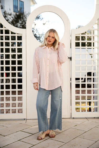 Woman standing in front of a white lattice gate wearing a striped shirt and jeans.