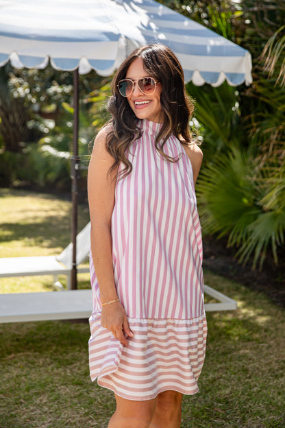 Woman wearing a pink and white striped dress standing outdoors under an umbrella.