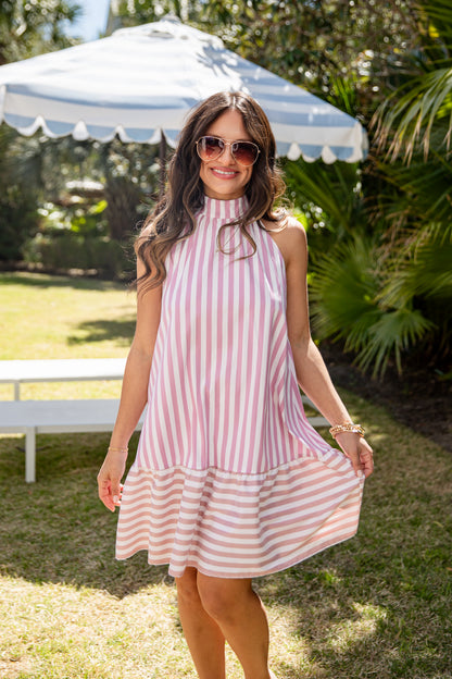 Woman wearing a pink and white striped dress outdoors under an umbrella.