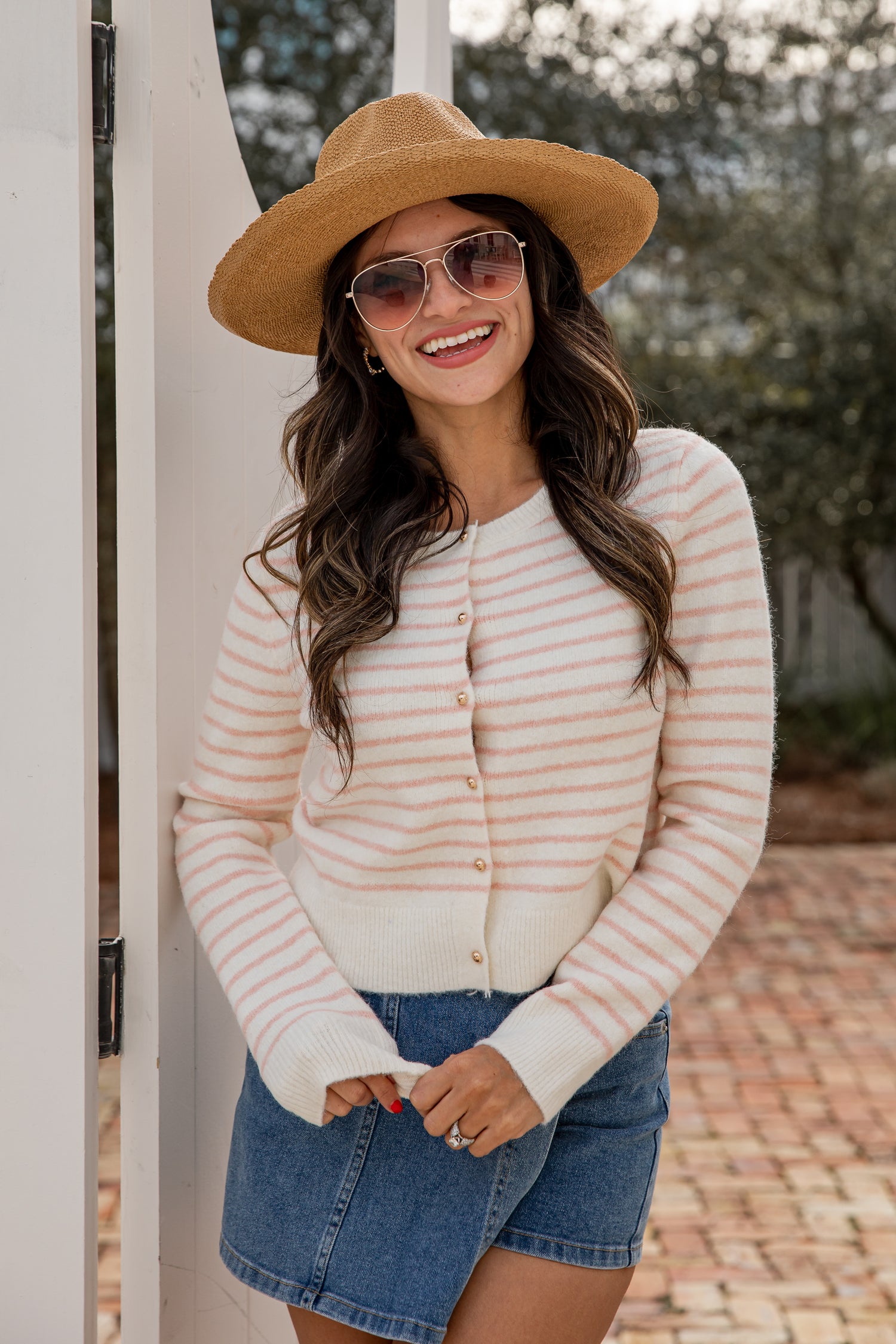 Woman wearing a striped sweater, denim shorts, and a hat outdoors.