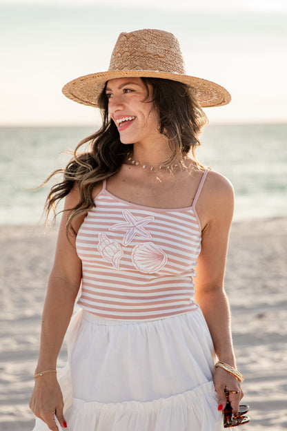 Woman on a beach wearing a striped tank top and wide-brimmed hat.