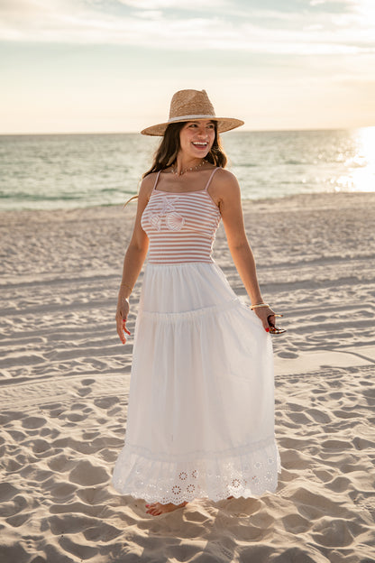 Woman in a striped dress and sun hat standing on a sandy beach.