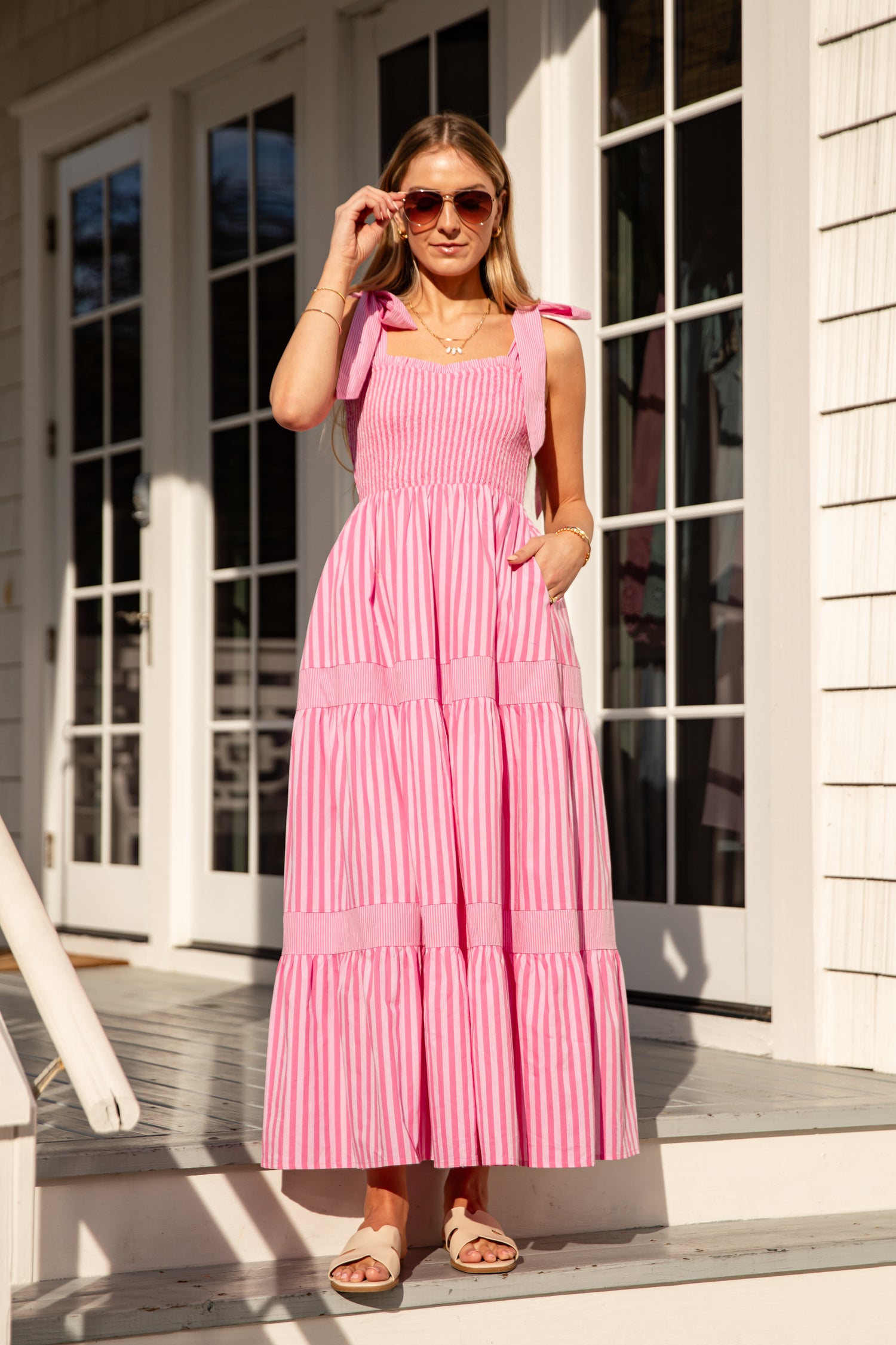 Woman wearing a pink striped dress standing on a porch.