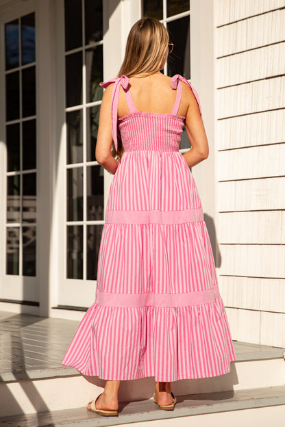 Woman wearing a pink dress with ruffled straps, standing in front of a white building.